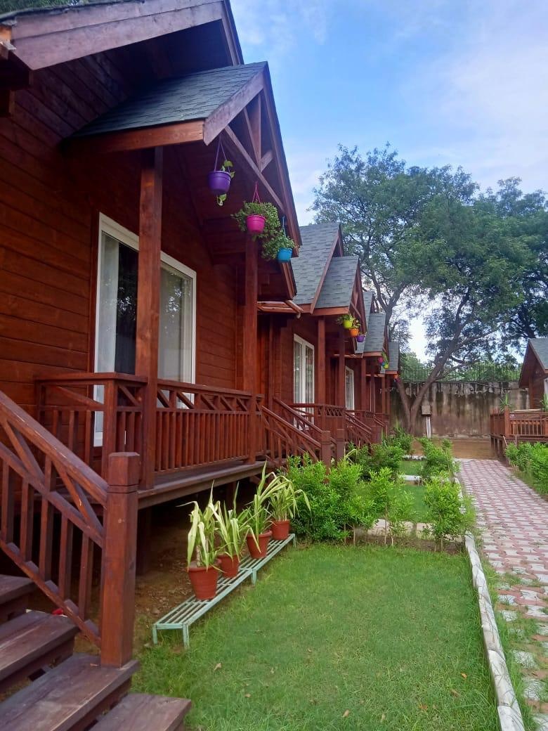 Farmhouse in Greater Noida for a party: wooden farm-stay cottages with a green lawn, potted plants and a garden path